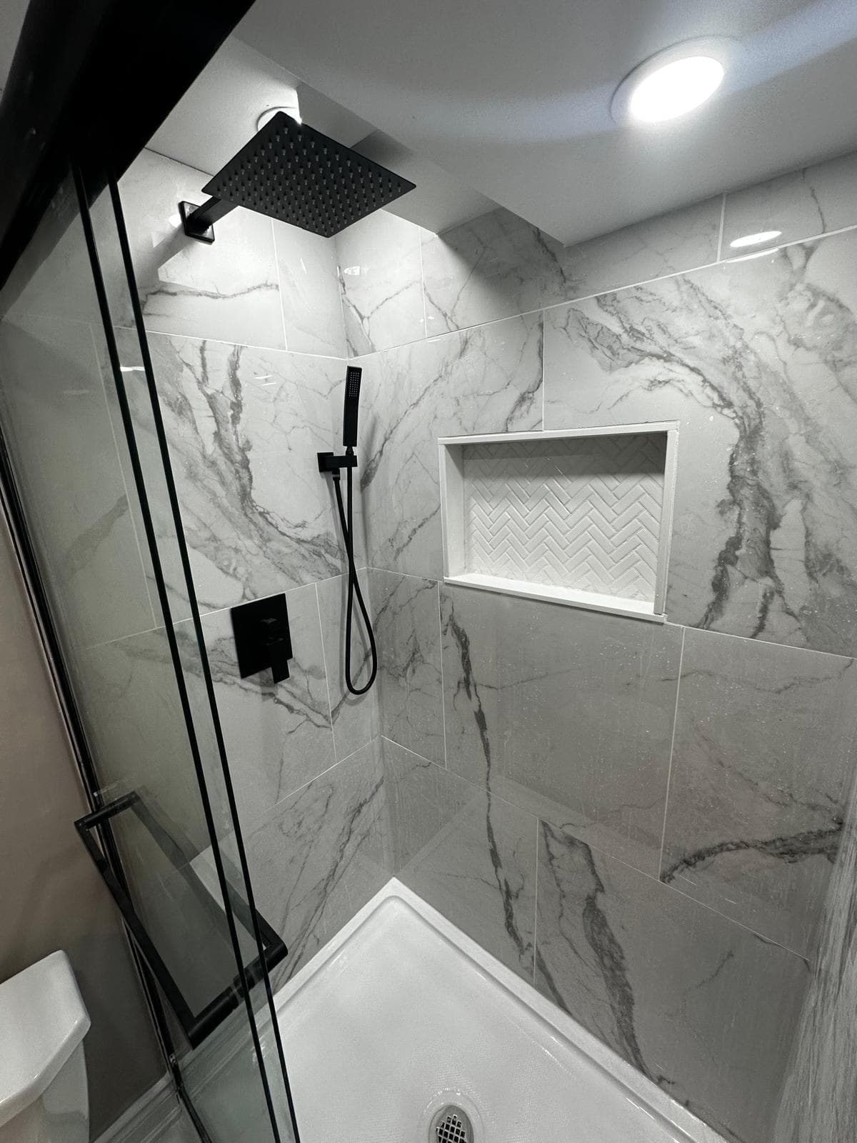 Marble bathroom shower with black sliding glass door, niche storage, and clean tile finish