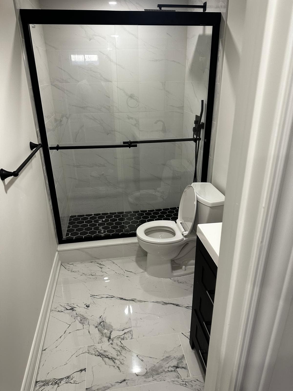 Modern bathroom with black-trim shower, marble walls, and black hexagon tile floor