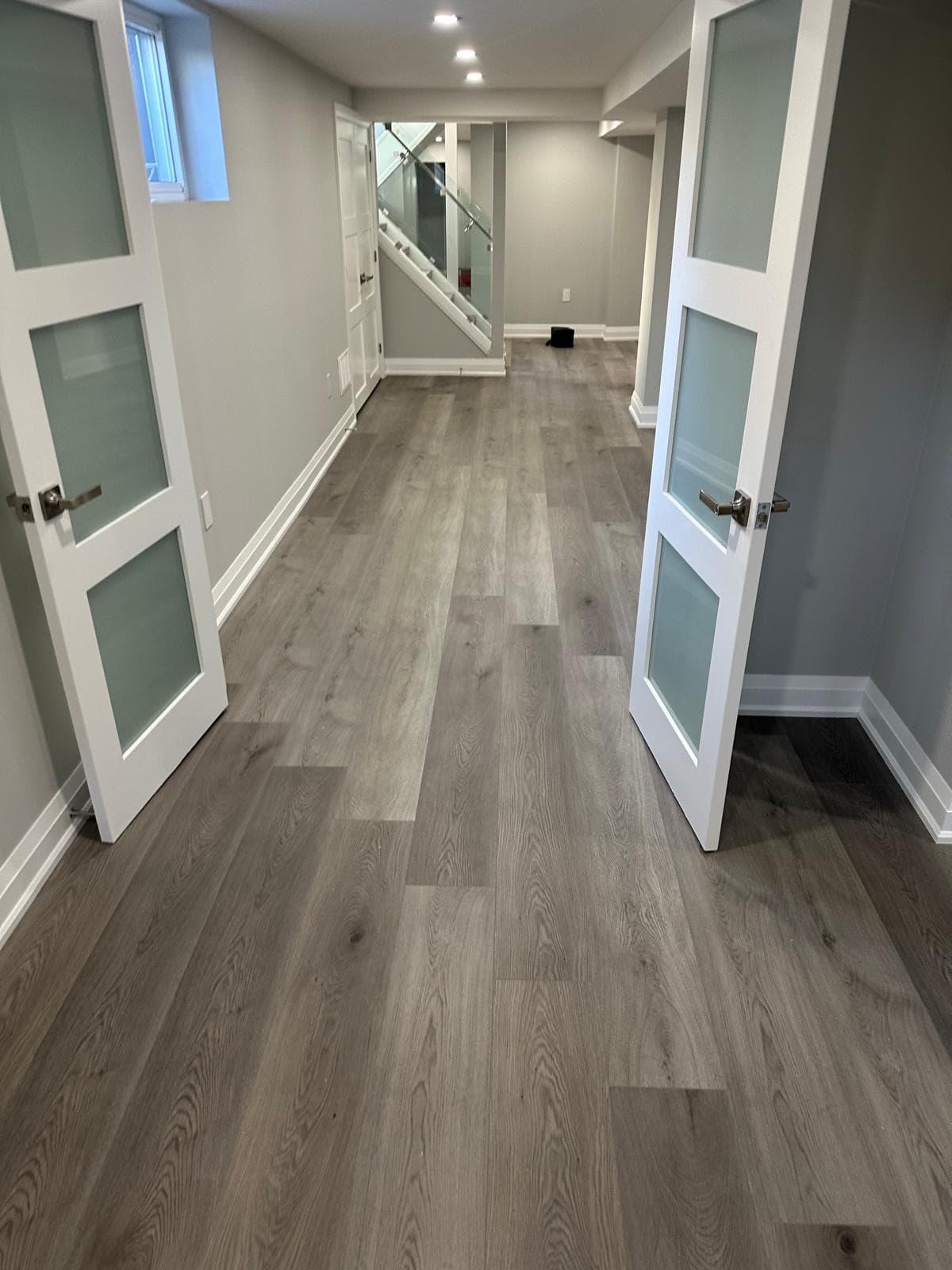 Toronto basement hallway with wide-plank flooring and frosted-glass french doors