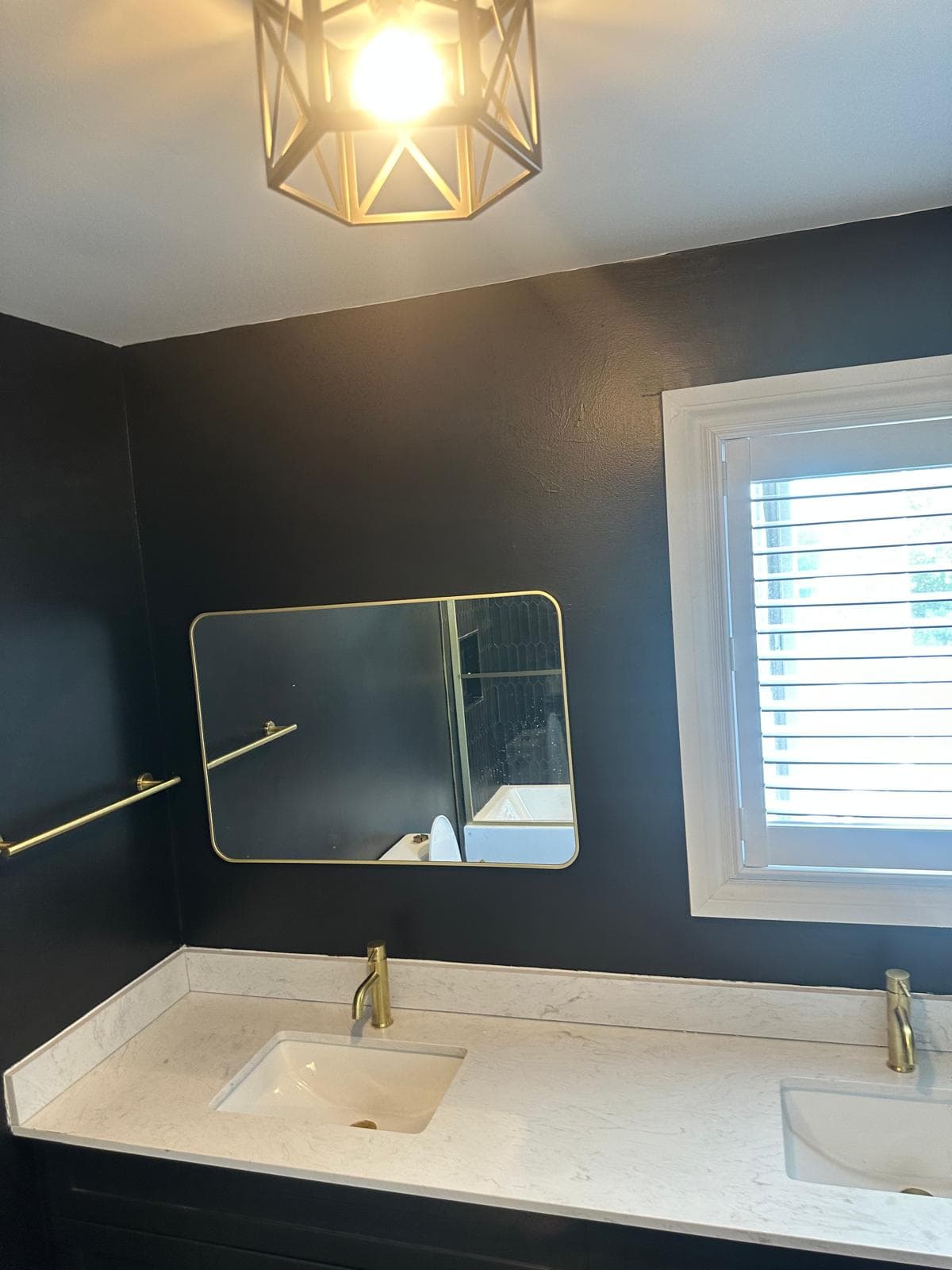 Black bathroom walls with gold-framed mirror, towel bar, and white vanity counter