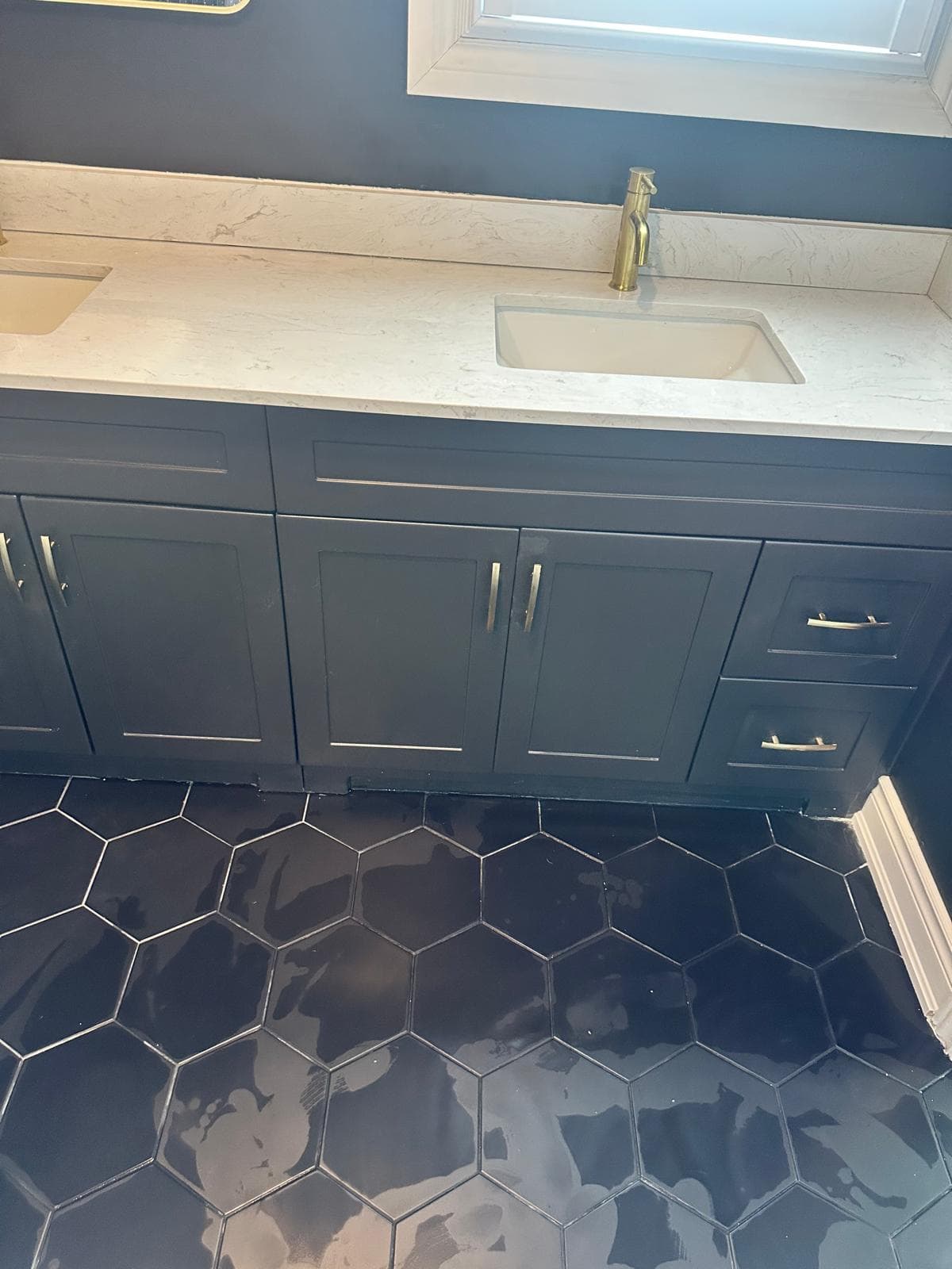 Dark double-sink vanity with white counter above the black hex tile floor
