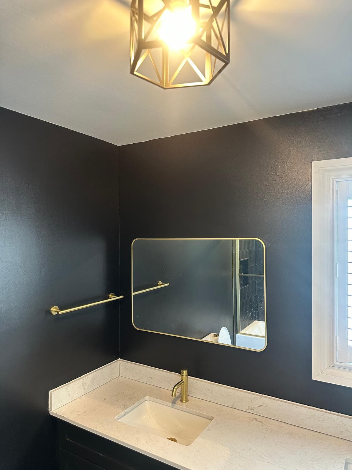 Corner vanity with gold mirror, towel bar, and black geometric ceiling light