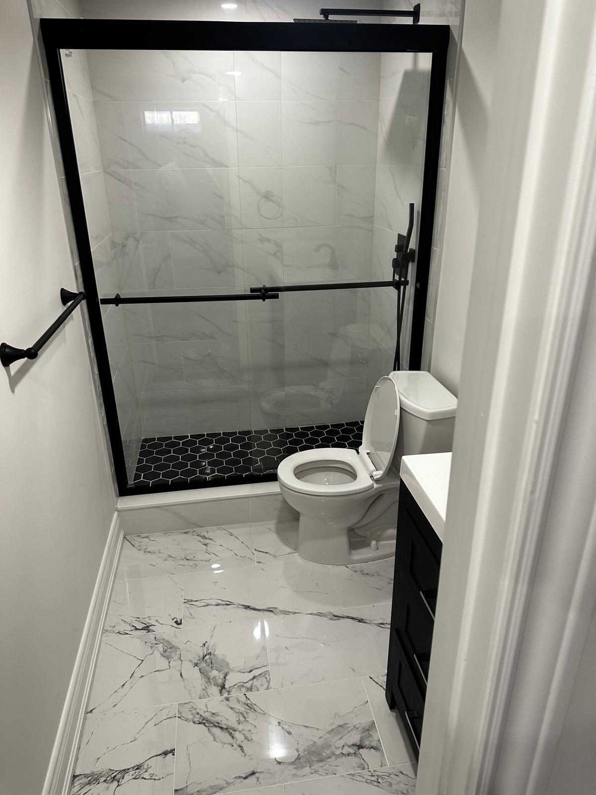 Modern bathroom with black-trim shower, marble walls, and black hexagon tile floor